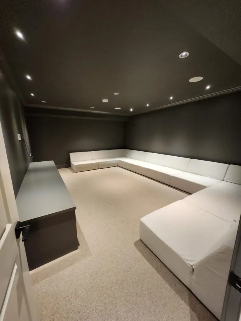 A dark TV room with a large u-shaped sofa in a lighter colour