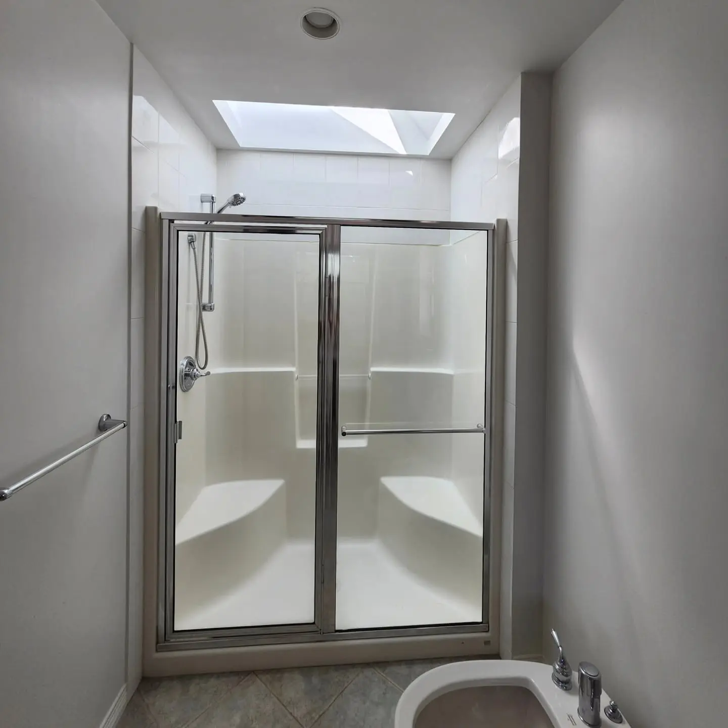 Bright bathroom shower with glass sliding doors, white walls and skylight providing natural light.